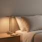Lampe de chevet design italien rechargeable argentée allumée sur table de nuit, éclairage LED chaud dans une chambre adulte minimaliste et élégante