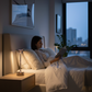 Femme lisant dans son lit éclairée par sa lampe de chevet design italien rechargeable argentée, ambiance lecture nocturne cosy dans une chambre adulte moderne