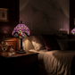 Lampe de chevet Vintage Tiffany violette avec abat-jour en vitraux colorés, posée sur une table de nuit dans une chambre.